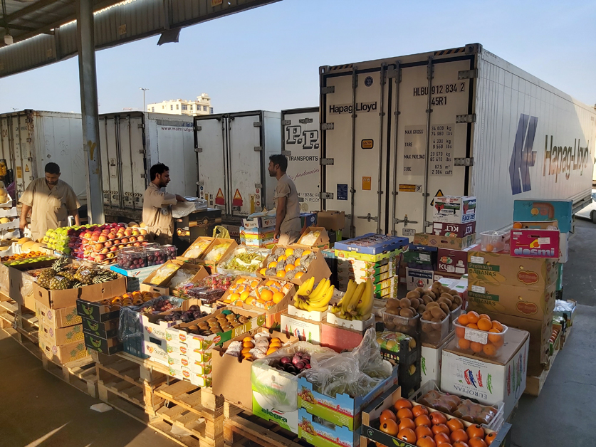 Photo of men with fresh fruits displayed behind trucks in a Jeddah market