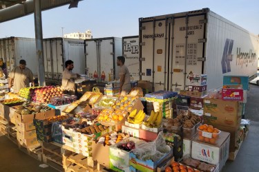 Photo of men with fresh fruits displayed behind trucks in a Jeddah market